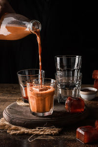 Close-up of coffee pouring in drinking glass on table against black background