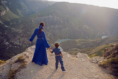 Mother in a blue dress with her son stands on the cliff of the sulak canyon