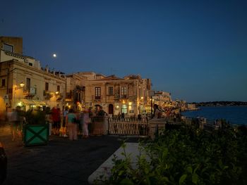 People in illuminated building against sky at dusk