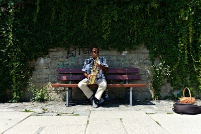 Full length portrait of man sitting on bench in park