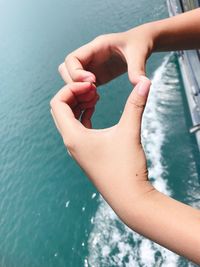 Cropped hands making heart shape over sea