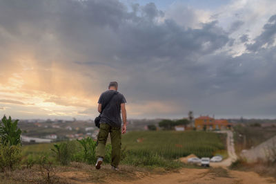 Rear view of man standing on field against sky during sunset