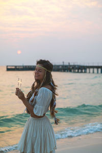 Portrait of young woman standing against sea during sunset