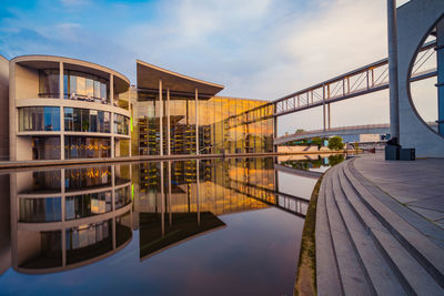 Reflection of modern buildings in lake against sky