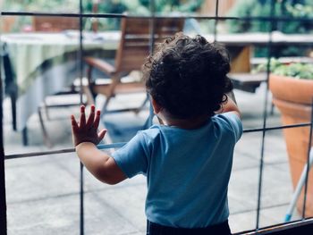 Rear view of boy standing by glass window