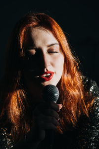 Portrait of redhead female singer woman in sparkly evening dress holding microphone on dark night