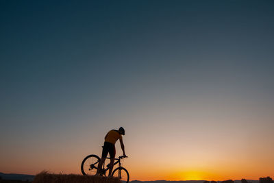Silhouette man riding bicycle against sky during sunset