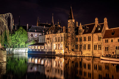 Bridge over river against buildings at night