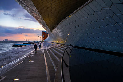 Man on bridge against sky in city during sunset