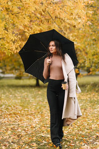 A beautiful cheerful girl walks under an umbrella in rainy weather in an autumn park in nature