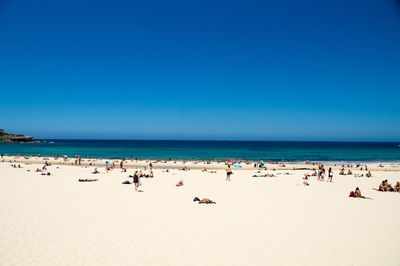 Group of people on beach against clear blue sky