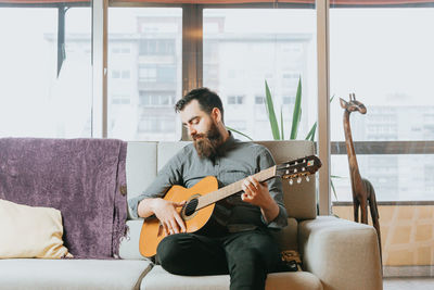 Young man playing guitar while sitting on sofa at home