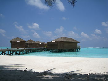 Stilt houses by pier over sea against sky