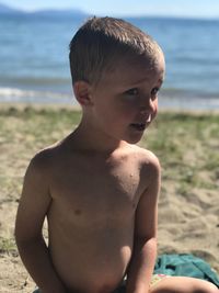 Close-up of wet shirtless boy sitting at beach