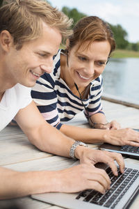 Happy mature woman with man using laptop on pier