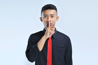 Young asian business man asking to be quiet with finger on lips. silence and secret concept