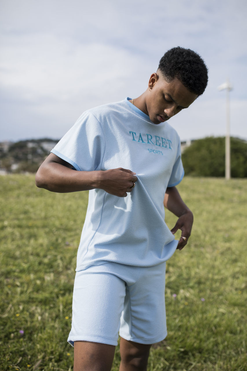 grass, one person, land, three quarter length, real people, field, day, young adult, leisure activity, lifestyles, young men, focus on foreground, nature, men, casual clothing, standing, front view, plant, males, outdoors, teenage boys, teenager