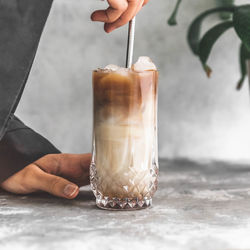 Midsection of person holding straw in iced coffee on table