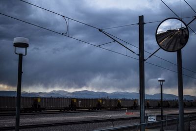 Electricity pylon by railroad tracks against sky