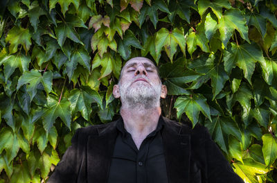 Portrait of adult man in black suit standing against green leaves