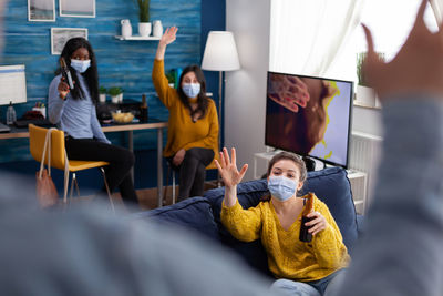 Cheerful people wearing mask drinking beer while watching tv at home