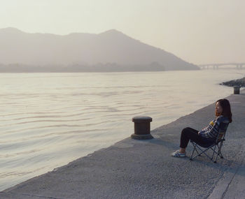 Man sitting at beach against sky