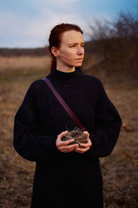 Portrait of young woman standing on field and holding a bird's nest