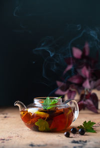 A teapot with black tea with currant berries, lemon, a cinnamon stick. autumn background. 