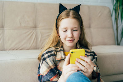Cute girl using mobile phone on sofa at home