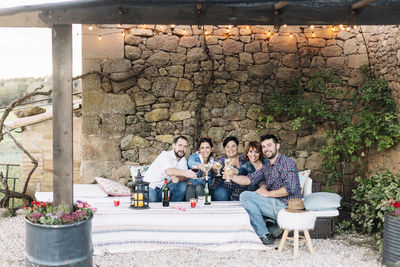 Portrait of friends doing celebratory toast against stone wall in yard