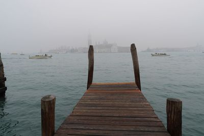 Wooden pier over river in city during foggy weather