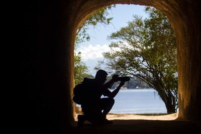 Silhouette man sitting by tree against sky