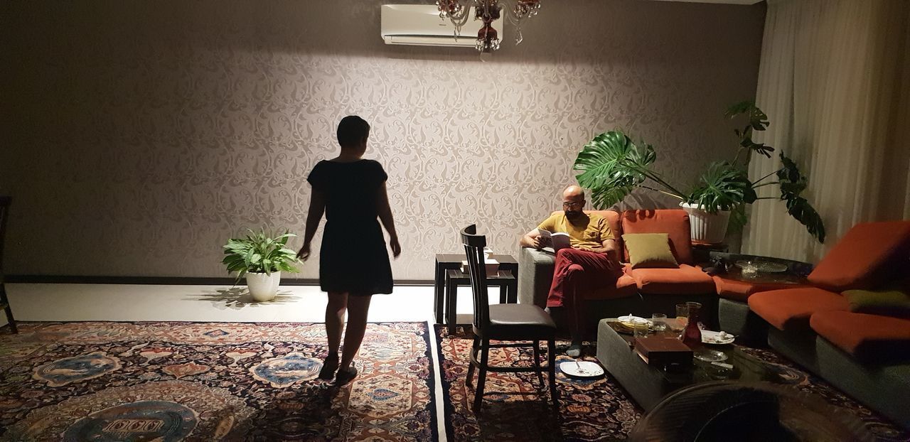 WOMAN SITTING ON TABLE BY POTTED PLANTS AT HOME