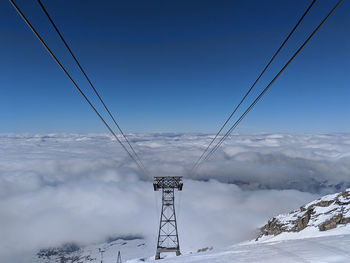 Electricity pylon on snow covered mountain against sky