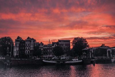 Sailboats in river by buildings against sky during sunset