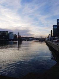 Bridge over river by buildings against sky at sunset