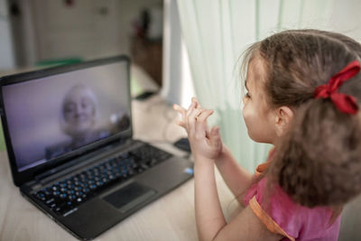 Cute girl talking with grandmother within video chat on laptop, digital conversation, self-isolation