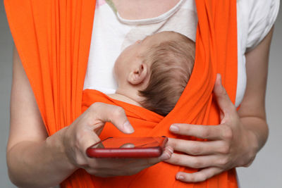 Crop mother with baby in sling holding smartphone