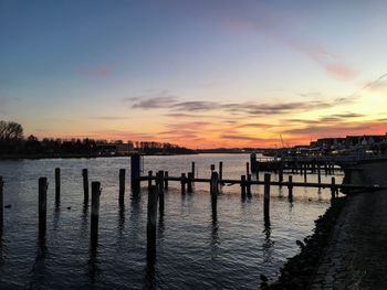 Silhouette wooden posts in sea against sky during sunset