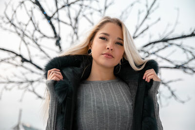 Portrait of beautiful woman standing against bare trees during winter