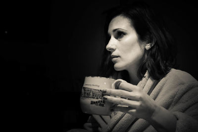 Thoughtful woman having coffee cup against black background