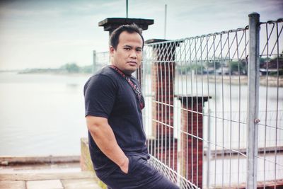 Young man looking away while standing by railing