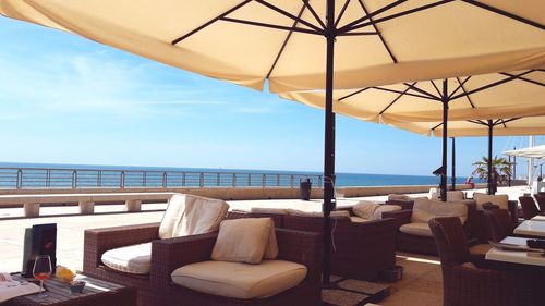 Deck chairs and parasols by sea against sky