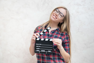 Portrait of woman holding film slate while standing against wall