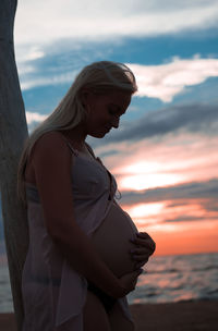 Side view of woman standing against sea at sunset