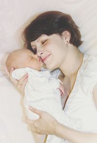 Smiling mother carrying baby while lying on bed at home