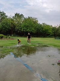 Father and son playing by pond against cloudy sky