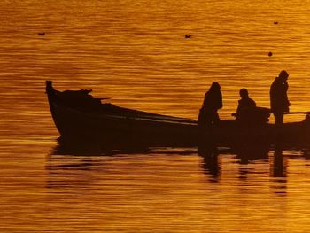 Silhouette people in lake against orange sky