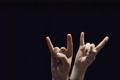Cropped hands of friends gesturing horn sign against black background