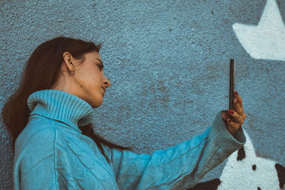 Portrait of teenage girl holding mobile phone against wall